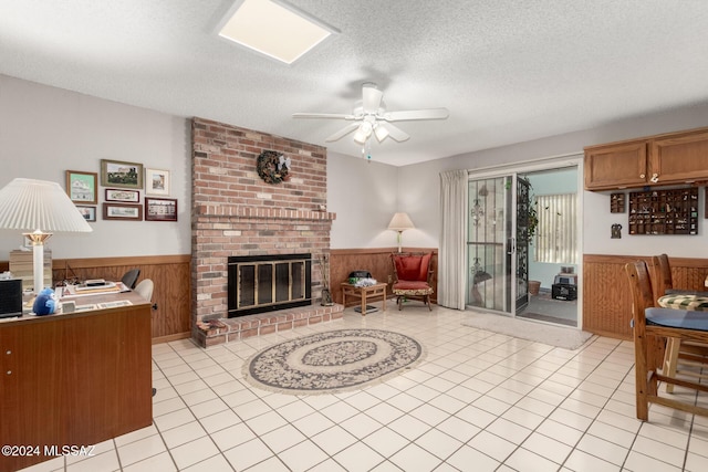 living room with ceiling fan, a textured ceiling, wooden walls, a fireplace, and light tile patterned flooring