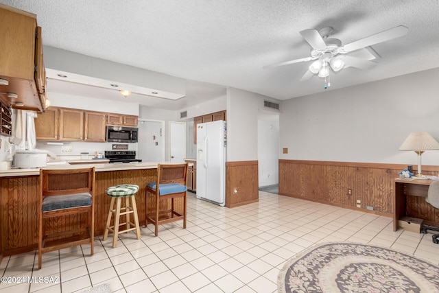 kitchen featuring white refrigerator with ice dispenser, black range oven, wooden walls, a kitchen bar, and kitchen peninsula