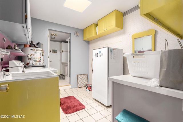 kitchen featuring light brown cabinetry, washer and clothes dryer, water heater, light tile patterned floors, and white refrigerator