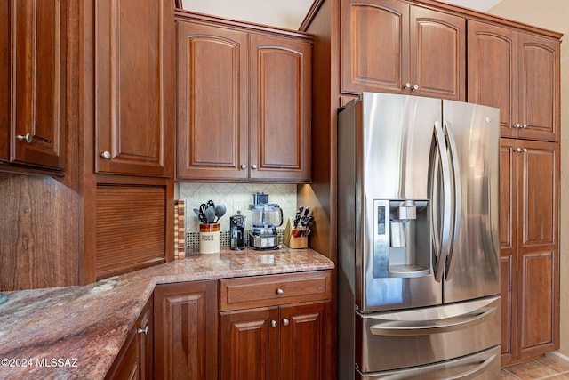 kitchen with light stone countertops, tasteful backsplash, stainless steel refrigerator with ice dispenser, and brown cabinets