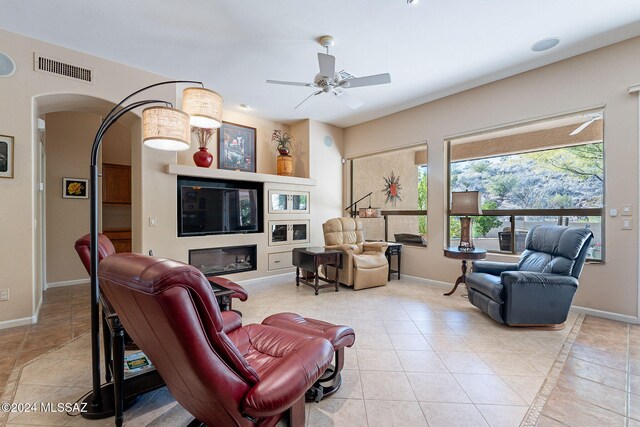 tiled living area featuring baseboards, ceiling fan, visible vents, and arched walkways