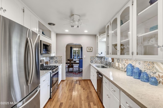 kitchen with sink, white cabinets, decorative backsplash, stainless steel appliances, and light wood-type flooring