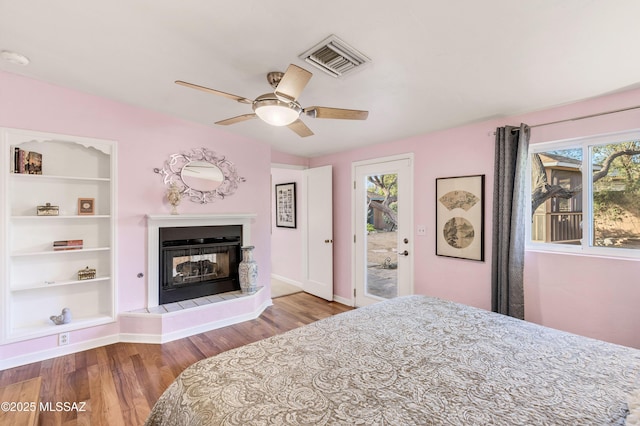 bedroom featuring ceiling fan, a tiled fireplace, light hardwood / wood-style floors, and access to outside