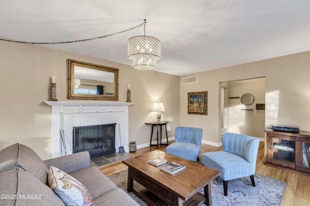 living room with a tiled fireplace, hardwood / wood-style floors, and a notable chandelier