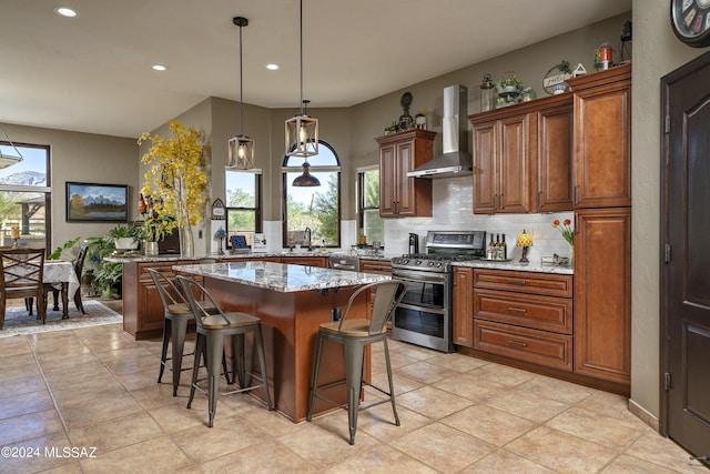 kitchen with double oven range, wall chimney exhaust hood, a wealth of natural light, a kitchen island, and light stone counters