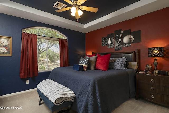 carpeted bedroom featuring multiple windows, a raised ceiling, and ceiling fan