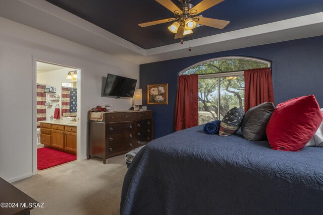 carpeted bedroom with a raised ceiling, ensuite bath, and ceiling fan