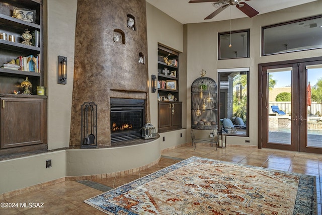 tiled living room with a large fireplace, built in shelves, ceiling fan, and french doors