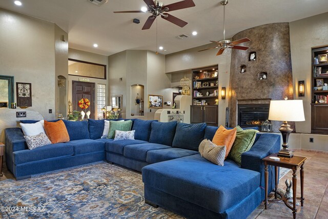 living room featuring built in shelves, a large fireplace, a towering ceiling, and ceiling fan