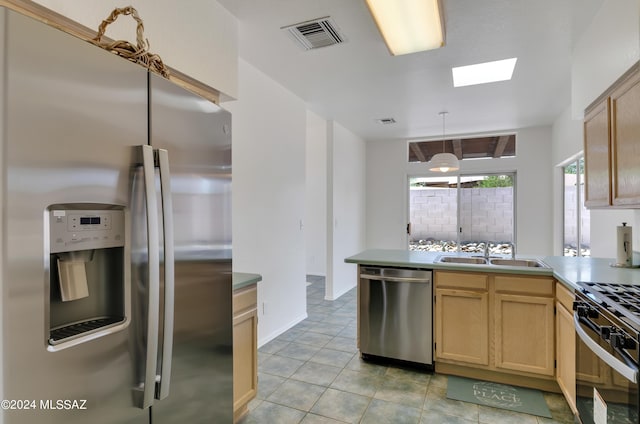 kitchen featuring sink, stainless steel appliances, light brown cabinetry, and a skylight