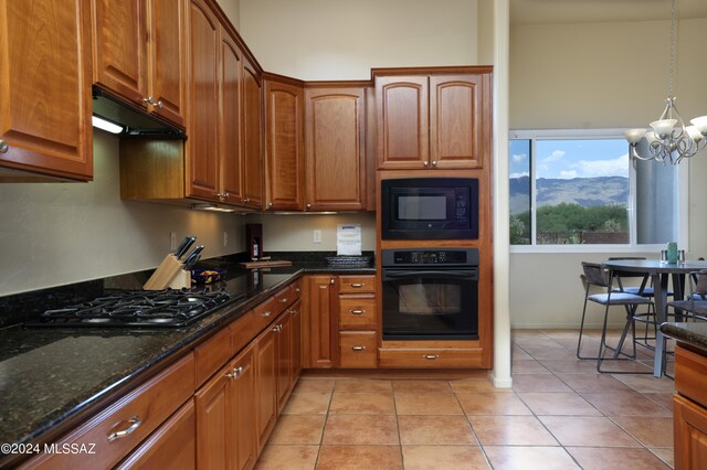 kitchen featuring black appliances, dark stone counters, under cabinet range hood, brown cabinets, and a notable chandelier