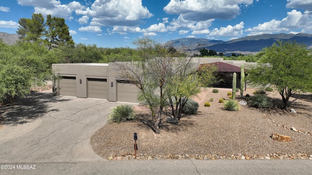 pueblo-style house featuring stucco siding, an attached garage, a mountain view, and aphalt driveway