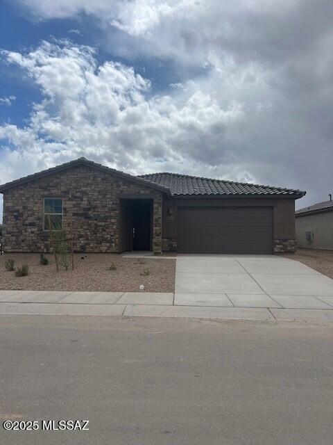 view of front of house with stone siding, a tile roof, concrete driveway, and an attached garage