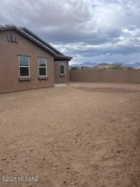 back of property with a tile roof, a mountain view, stucco siding, and fence