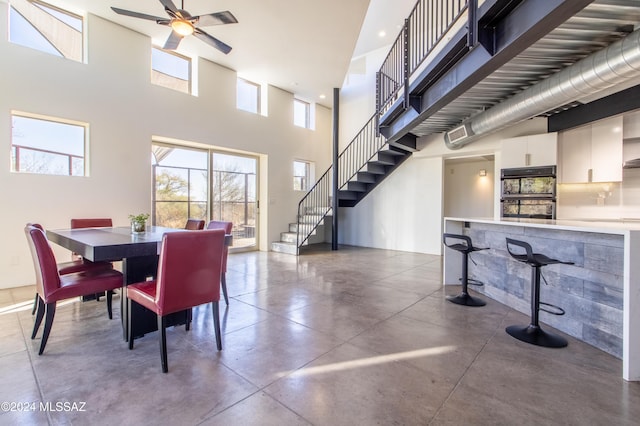 dining area featuring a high ceiling, concrete flooring, and ceiling fan