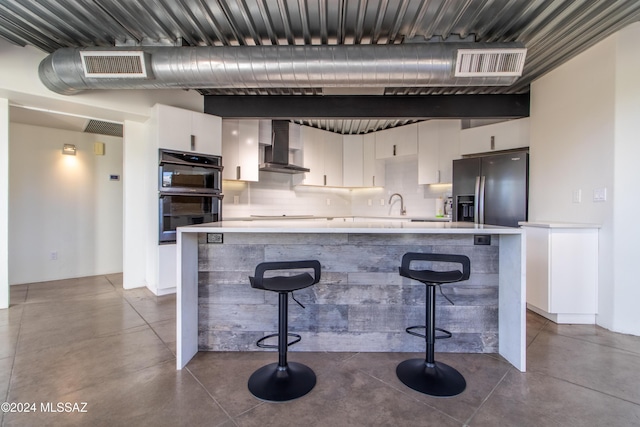 kitchen featuring a kitchen breakfast bar, double oven, wall chimney exhaust hood, stainless steel refrigerator with ice dispenser, and white cabinets