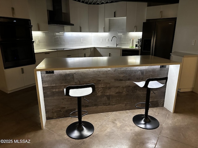 kitchen with black appliances, wall chimney range hood, decorative backsplash, and sink