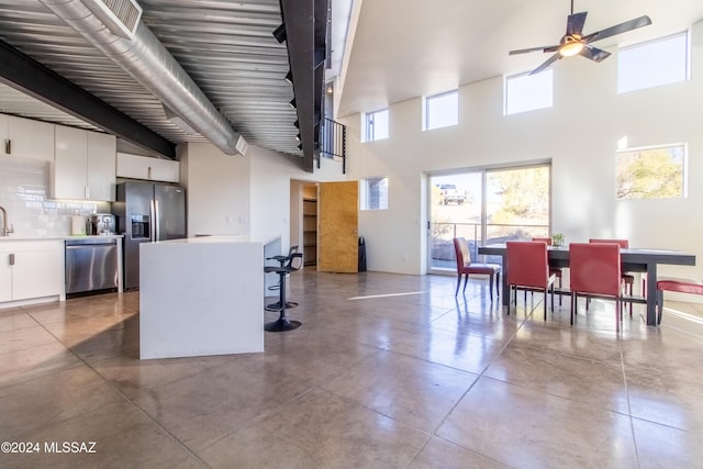 kitchen with stainless steel appliances, ceiling fan, concrete flooring, white cabinetry, and tasteful backsplash