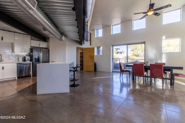 kitchen featuring appliances with stainless steel finishes, ceiling fan, a kitchen bar, white cabinets, and backsplash