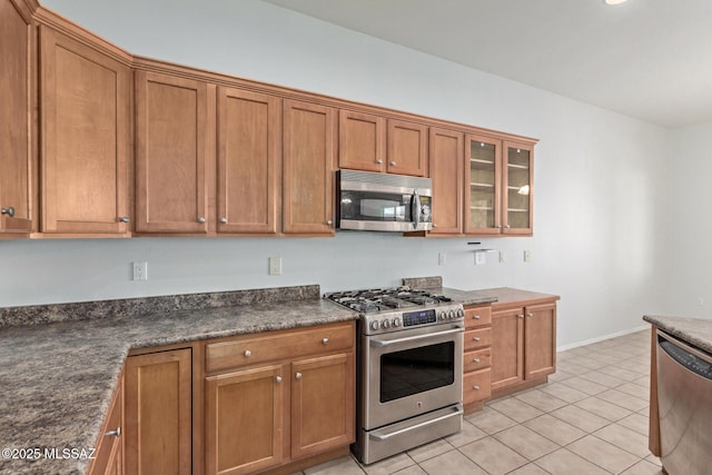 kitchen with stainless steel appliances, dark stone counters, and light tile patterned floors