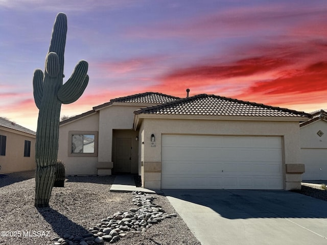 view of front of house featuring an attached garage, a tiled roof, concrete driveway, and stucco siding