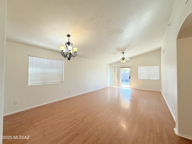 spare room with ceiling fan with notable chandelier, vaulted ceiling, and light hardwood / wood-style flooring