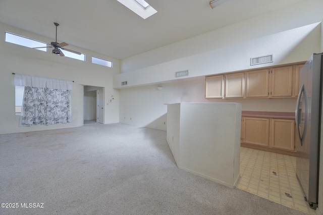 empty room with ceiling fan, light carpet, a high ceiling, and a skylight