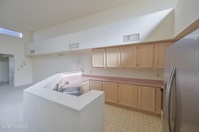 kitchen featuring kitchen peninsula, stainless steel fridge, sink, light brown cabinets, and tile counters