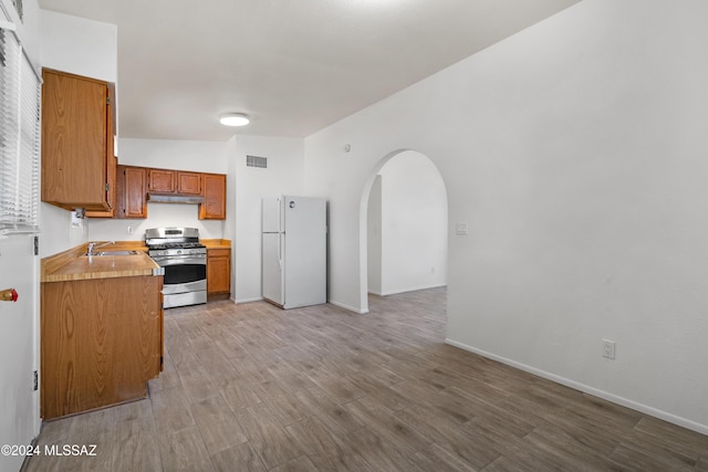 kitchen with sink, white fridge, light hardwood / wood-style floors, and stainless steel range with gas stovetop