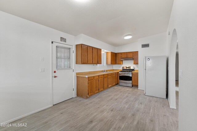 kitchen with white fridge, stainless steel range with gas cooktop, sink, and light hardwood / wood-style flooring