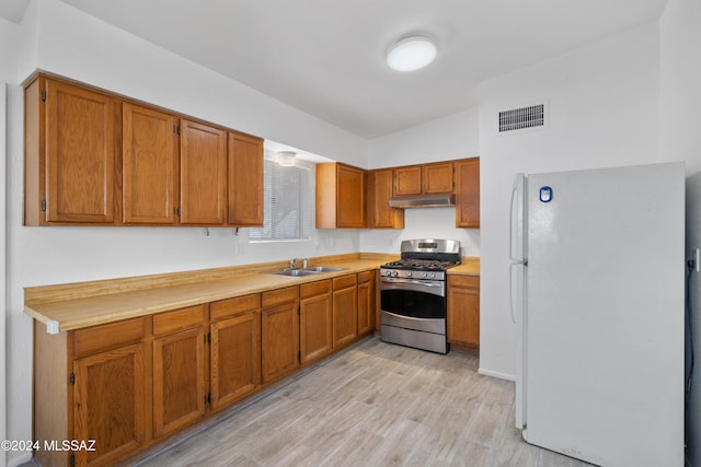 kitchen featuring gas stove, white fridge, light hardwood / wood-style flooring, and sink