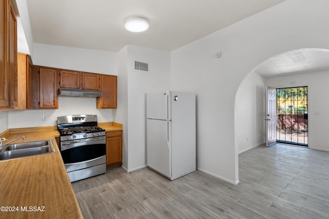 kitchen featuring stainless steel gas range oven, white fridge, light hardwood / wood-style floors, and sink