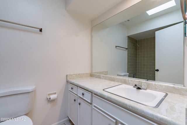 bathroom featuring tiled shower, vanity, a skylight, and toilet