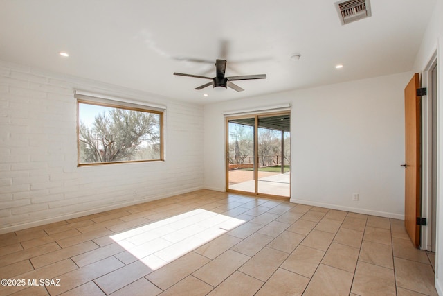 empty room featuring ceiling fan and brick wall