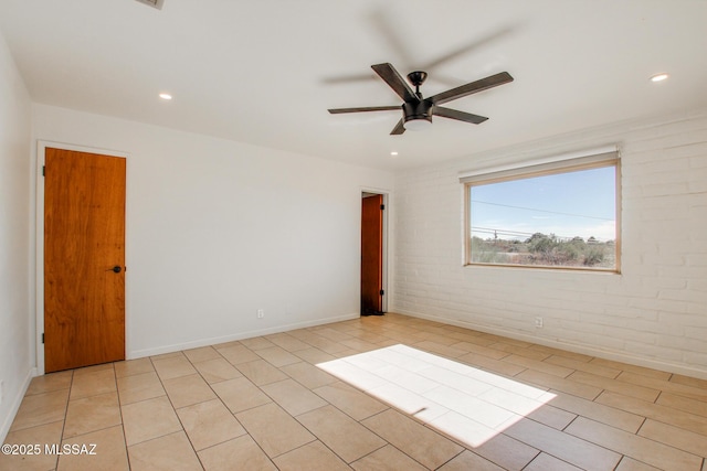 tiled empty room featuring ceiling fan and brick wall