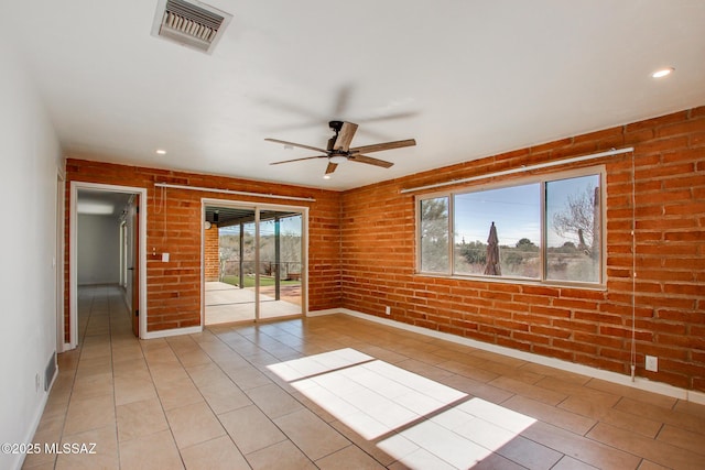 unfurnished room featuring ceiling fan, a healthy amount of sunlight, and brick wall