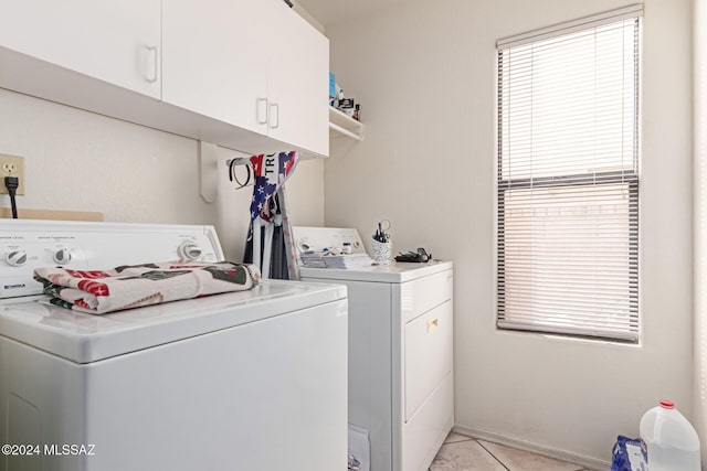 laundry area featuring washing machine and clothes dryer, a healthy amount of sunlight, light tile patterned flooring, and cabinets