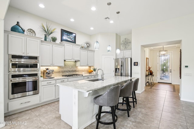 kitchen featuring pendant lighting, a kitchen island with sink, sink, appliances with stainless steel finishes, and white cabinetry