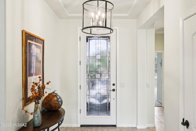 foyer entrance featuring a tray ceiling, light tile patterned flooring, and a notable chandelier