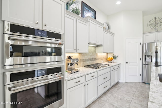 kitchen featuring white cabinetry, stainless steel appliances, light stone counters, backsplash, and light tile patterned floors