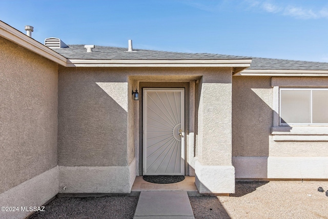 property entrance with a shingled roof and stucco siding