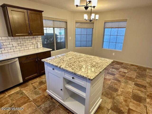 kitchen with decorative light fixtures, stainless steel dishwasher, a notable chandelier, light stone countertops, and backsplash