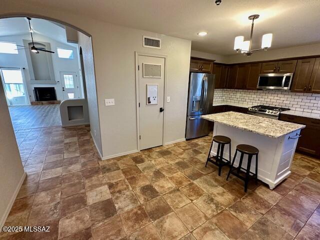 kitchen with pendant lighting, backsplash, ceiling fan with notable chandelier, appliances with stainless steel finishes, and a kitchen island