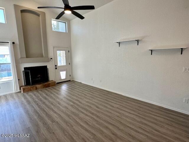 unfurnished living room with dark wood-type flooring, ceiling fan, and a high ceiling