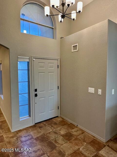 foyer entrance with a notable chandelier, a healthy amount of sunlight, and a towering ceiling