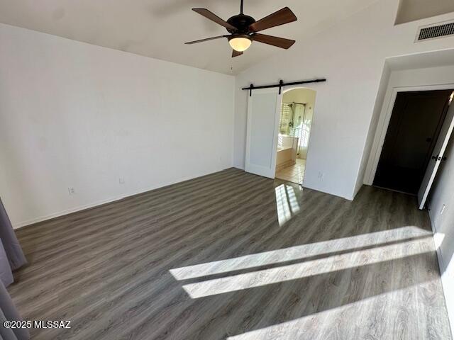 empty room featuring a barn door, vaulted ceiling, ceiling fan, and dark wood-type flooring