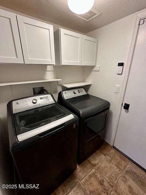 laundry room with cabinets, washer and dryer, and a textured ceiling