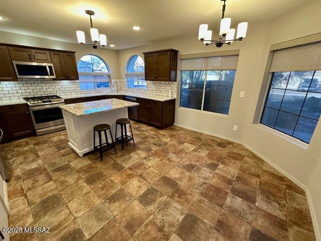 kitchen featuring tasteful backsplash, stainless steel appliances, decorative light fixtures, a chandelier, and a center island