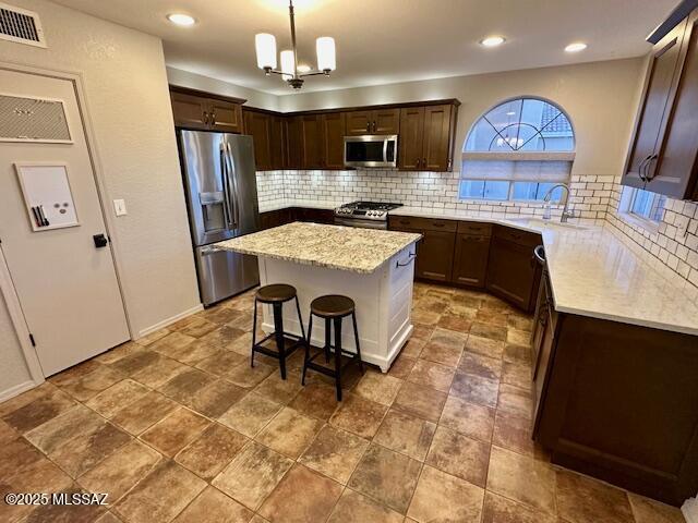 kitchen with tasteful backsplash, stainless steel appliances, a chandelier, a center island, and hanging light fixtures