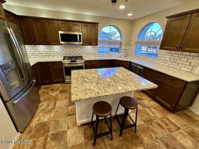 kitchen with sink, a center island, appliances with stainless steel finishes, a kitchen breakfast bar, and light stone countertops